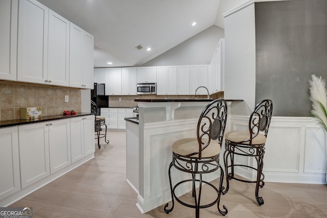 kitchen with white cabinets, vaulted ceiling, decorative backsplash, kitchen peninsula, and a breakfast bar area