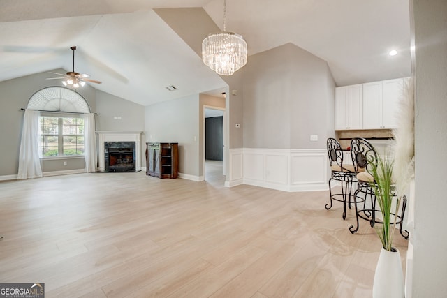 living room with a premium fireplace, ceiling fan with notable chandelier, lofted ceiling, and light wood-type flooring