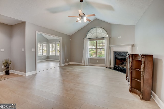 unfurnished living room with a wealth of natural light, a premium fireplace, lofted ceiling, and light wood-type flooring