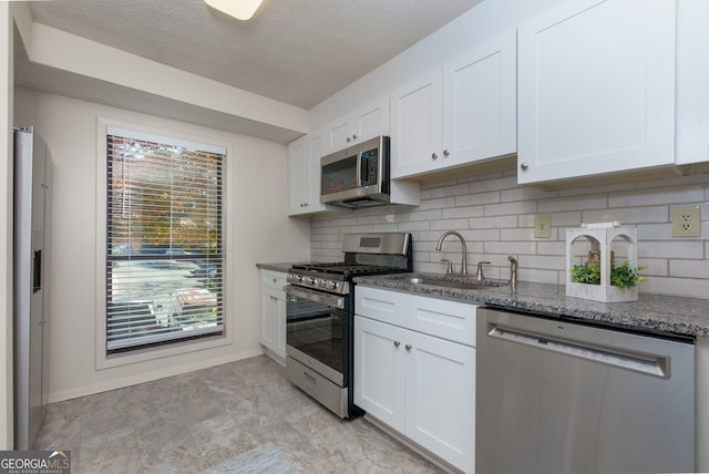 kitchen featuring decorative backsplash, dark stone countertops, white cabinets, stainless steel appliances, and a sink