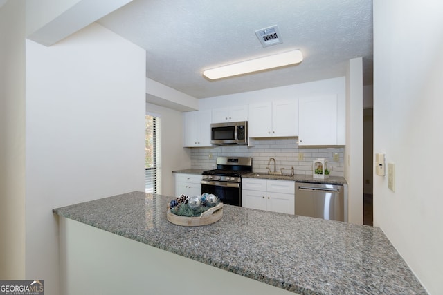 kitchen with white cabinets, sink, decorative backsplash, dark stone countertops, and stainless steel appliances