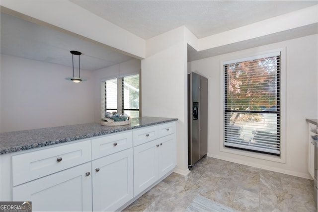 kitchen featuring a textured ceiling, pendant lighting, dark stone countertops, stainless steel fridge with ice dispenser, and white cabinetry