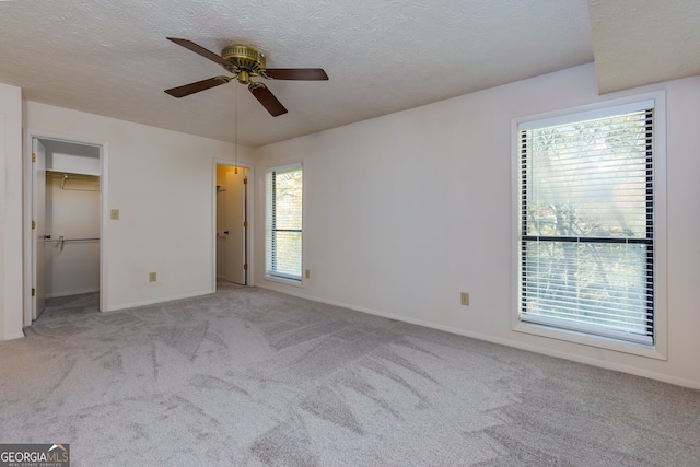 unfurnished bedroom with a walk in closet, ceiling fan, light carpet, and a textured ceiling