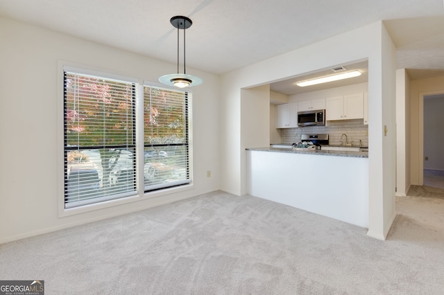 kitchen featuring backsplash, light carpet, white cabinets, appliances with stainless steel finishes, and decorative light fixtures