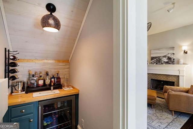 bar featuring wooden counters, a brick fireplace, vaulted ceiling, blue cabinets, and beverage cooler