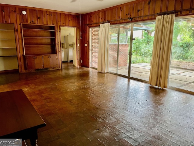 unfurnished living room featuring ceiling fan and wood walls