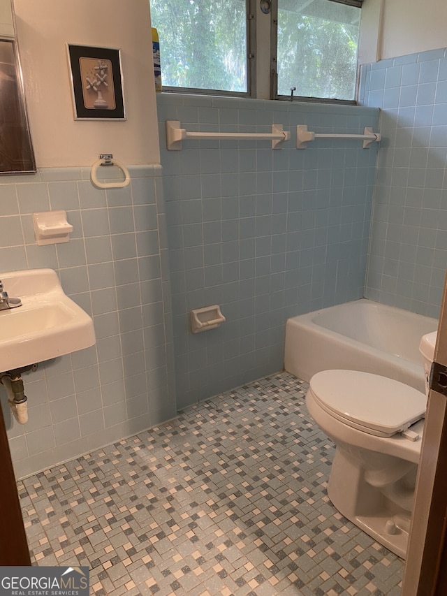 bathroom with tile patterned floors, toilet, a wealth of natural light, and tile walls