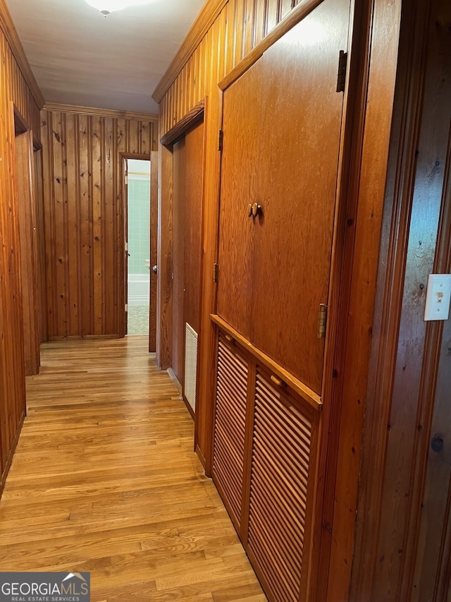 corridor featuring light wood-type flooring, ornamental molding, and wood walls