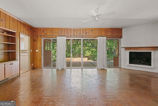 unfurnished living room featuring a brick fireplace, ceiling fan, and wooden walls