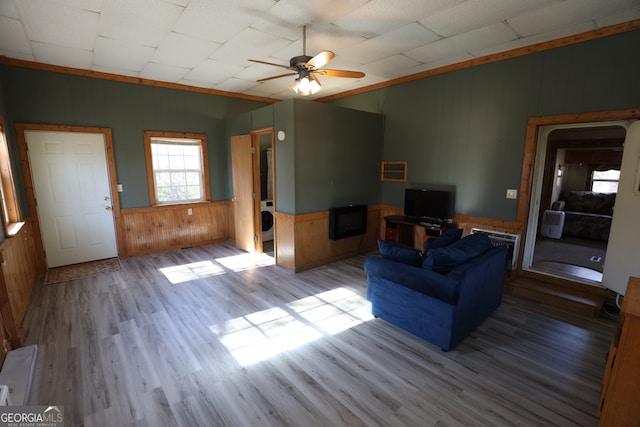 living room featuring ceiling fan, light hardwood / wood-style floors, wood walls, and washer / dryer