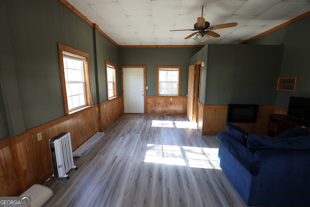 living room with wooden walls, light hardwood / wood-style flooring, ceiling fan, ornamental molding, and radiator heating unit