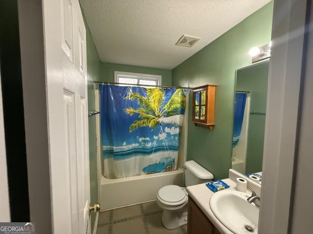 full bathroom with shower / bath combo, toilet, a textured ceiling, and vanity