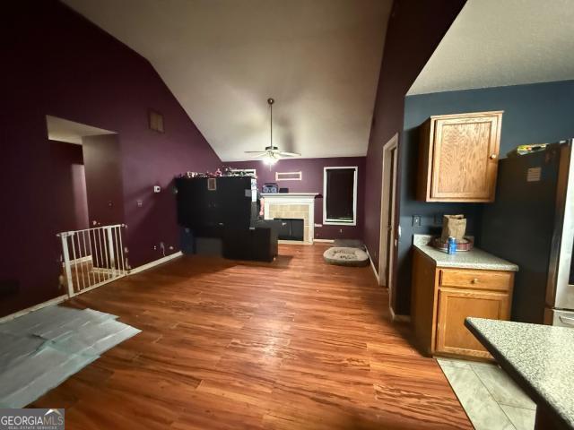 kitchen with high vaulted ceiling, black refrigerator, light hardwood / wood-style flooring, ceiling fan, and a fireplace