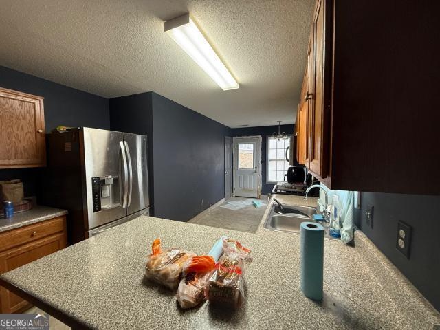 kitchen featuring sink, an inviting chandelier, stainless steel refrigerator with ice dispenser, kitchen peninsula, and a textured ceiling