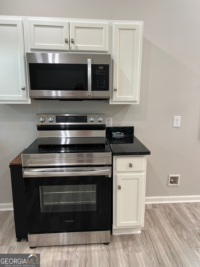 kitchen with dark stone countertops, white cabinets, light hardwood / wood-style floors, and appliances with stainless steel finishes