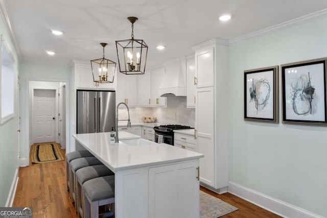 kitchen with stainless steel appliances, sink, white cabinetry, hanging light fixtures, and an island with sink