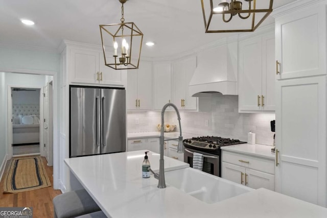 kitchen featuring appliances with stainless steel finishes, premium range hood, pendant lighting, hardwood / wood-style flooring, and white cabinets