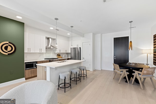 kitchen with appliances with stainless steel finishes, wall chimney exhaust hood, sink, light hardwood / wood-style floors, and white cabinetry