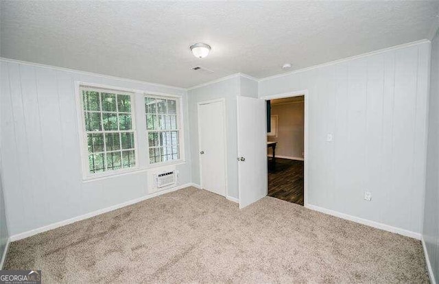 carpeted empty room featuring crown molding, a textured ceiling, and wooden walls