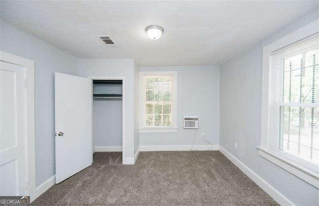 unfurnished bedroom with carpet floors, a textured ceiling, a wall unit AC, and a closet