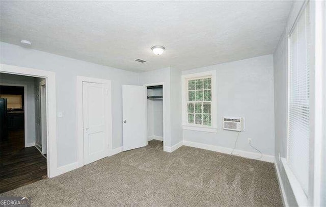 unfurnished bedroom with a wall mounted air conditioner, a textured ceiling, and carpet floors