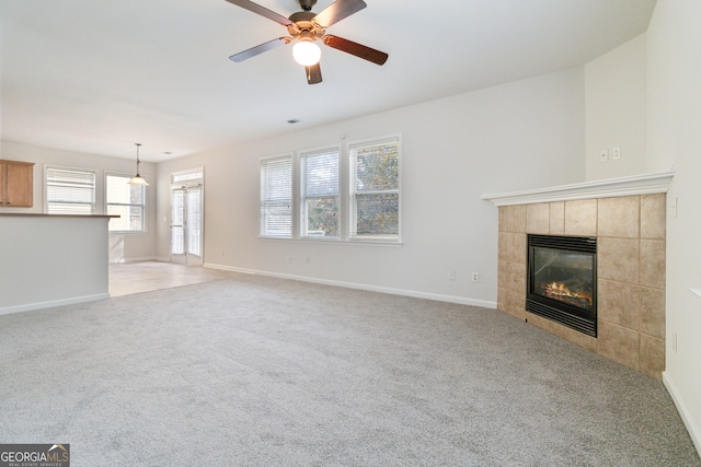 unfurnished living room featuring a tile fireplace, ceiling fan, and light colored carpet