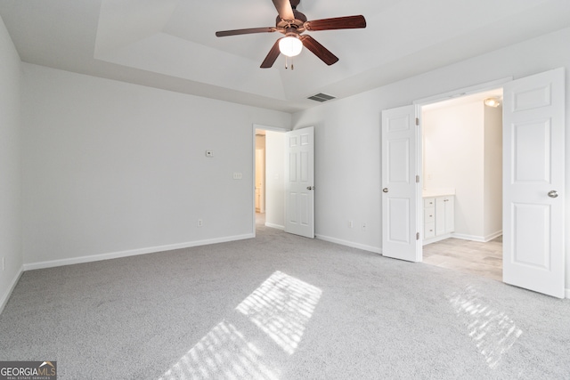 unfurnished bedroom with ceiling fan, light carpet, connected bathroom, and a tray ceiling