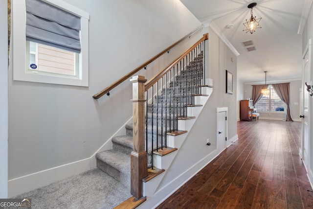 stairway featuring hardwood / wood-style flooring, crown molding, and an inviting chandelier