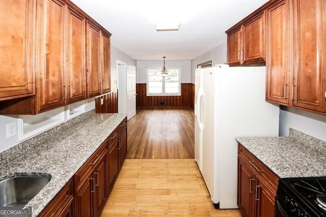 kitchen featuring light stone countertops, light wood-type flooring, sink, white refrigerator, and decorative light fixtures