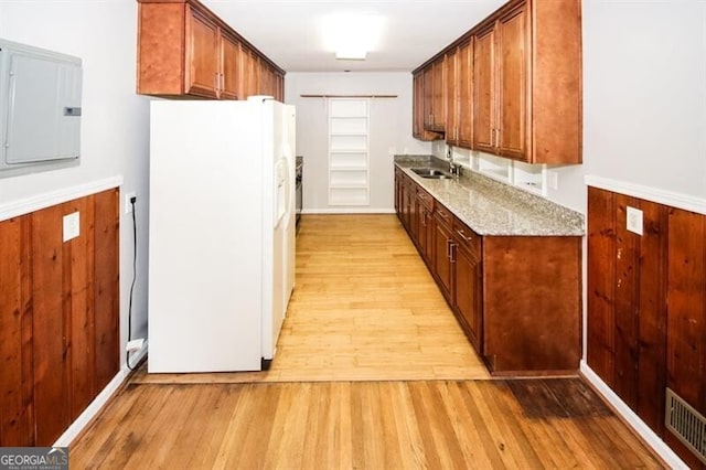 kitchen with light stone countertops, light hardwood / wood-style floors, sink, white refrigerator with ice dispenser, and electric panel