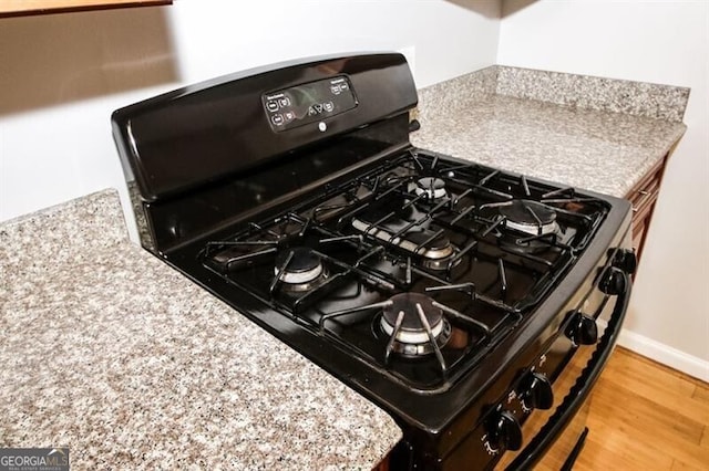 room details with light stone counters, wood-type flooring, and black range with gas cooktop