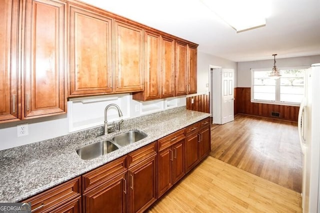 kitchen with light stone countertops, sink, hanging light fixtures, white refrigerator, and light wood-type flooring