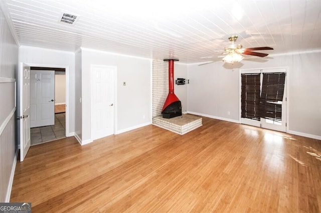 unfurnished living room with a wood stove, ceiling fan, and wood-type flooring