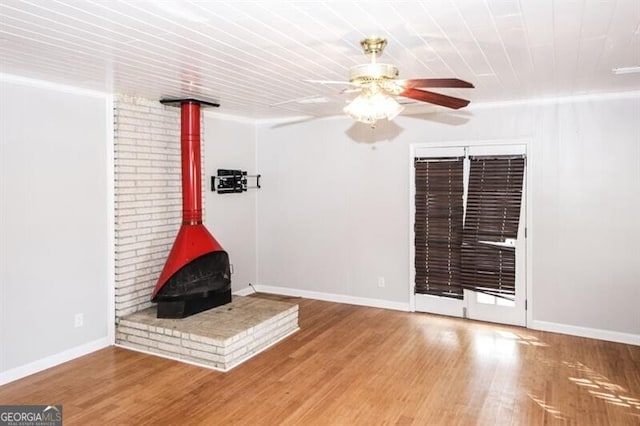 unfurnished living room with ceiling fan, wood-type flooring, a wood stove, and crown molding