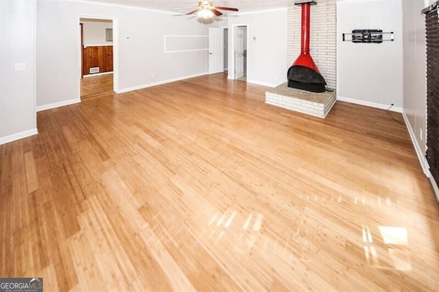 unfurnished living room with hardwood / wood-style floors, a wood stove, and ceiling fan