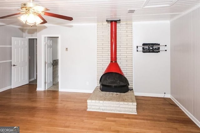 unfurnished living room with a wood stove, ceiling fan, hardwood / wood-style floors, and ornamental molding