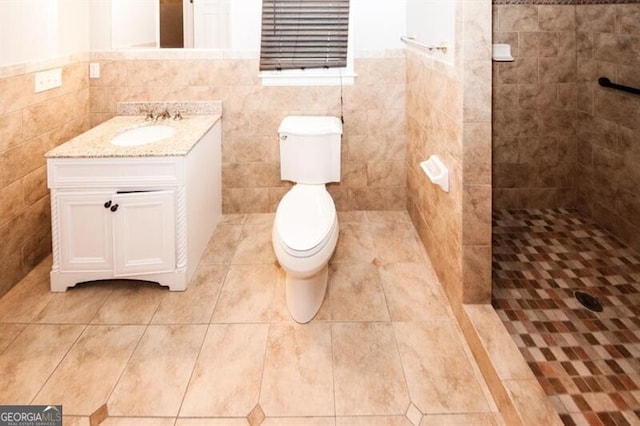 bathroom with a tile shower, vanity, tile walls, and toilet