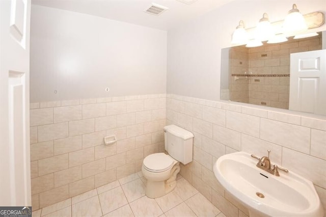 bathroom featuring tile patterned floors, toilet, sink, and tile walls