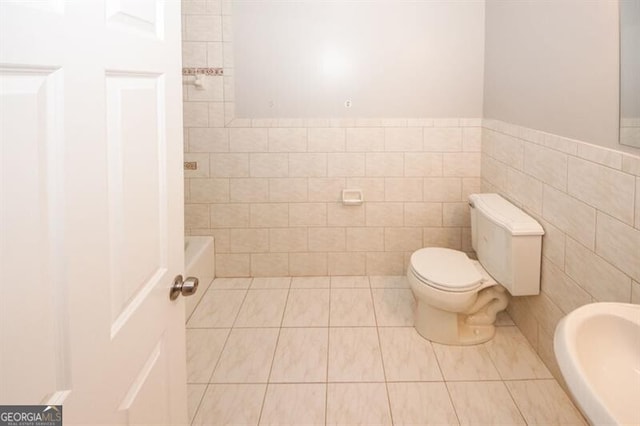 bathroom featuring a tub to relax in, tile patterned flooring, tile walls, and toilet