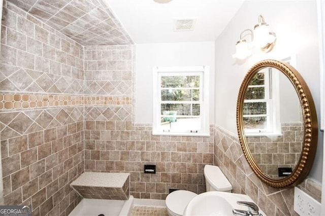 bathroom with tiled shower, toilet, plenty of natural light, and tile walls