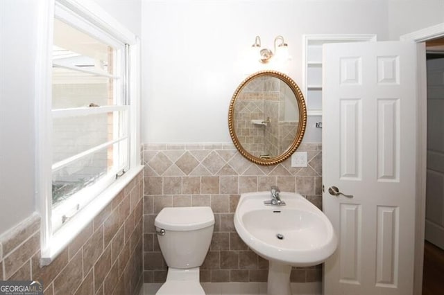 bathroom with sink, a healthy amount of sunlight, toilet, and tile walls