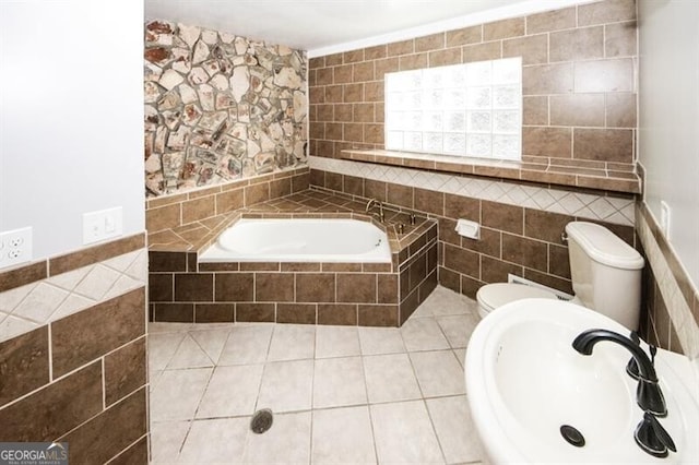 bathroom with sink, tile patterned flooring, tiled bath, toilet, and tile walls