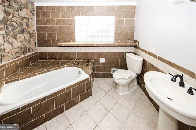 bathroom featuring sink, tile walls, tile patterned flooring, tiled bath, and toilet