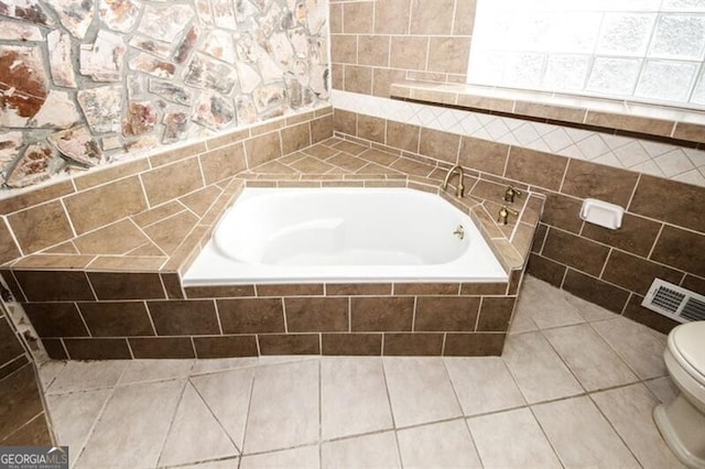 bathroom featuring tile patterned floors, a relaxing tiled tub, and toilet