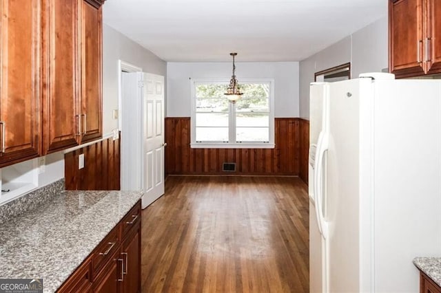 kitchen with white refrigerator with ice dispenser, decorative light fixtures, light stone countertops, and dark wood-type flooring