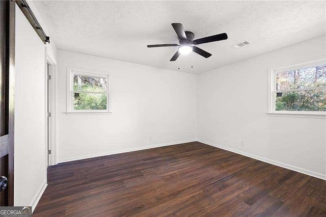 empty room with a barn door, ceiling fan, dark hardwood / wood-style floors, and a textured ceiling