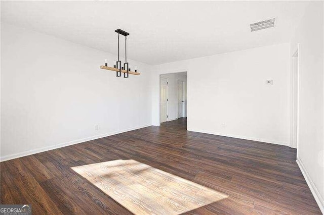 spare room with dark hardwood / wood-style floors and an inviting chandelier