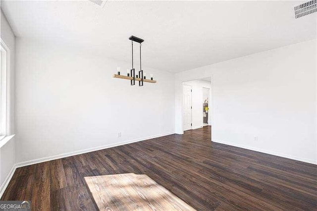 spare room with dark hardwood / wood-style floors and an inviting chandelier