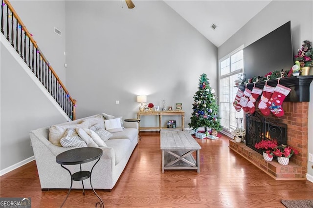 living room with a brick fireplace, high vaulted ceiling, and hardwood / wood-style flooring