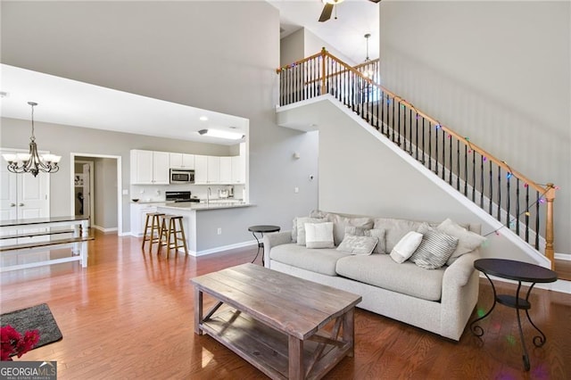 living room with sink, ceiling fan with notable chandelier, wood-type flooring, and a high ceiling